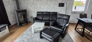 Gemütliches Wohnzimmer, frisch renoviert und neuer echt Holzboden Februar 2026 mit Sofa, Fernsehsessel mit Fußhocker und Kaminofen. - Bild 12: Nordsee Ferienhaus Dornumersiel strandnah - Hund willkommen - WLAN